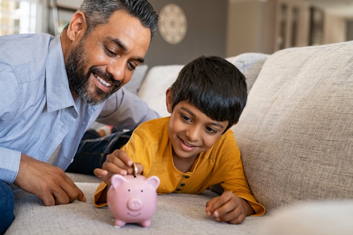 Dad helping son put money in a piggy bank.